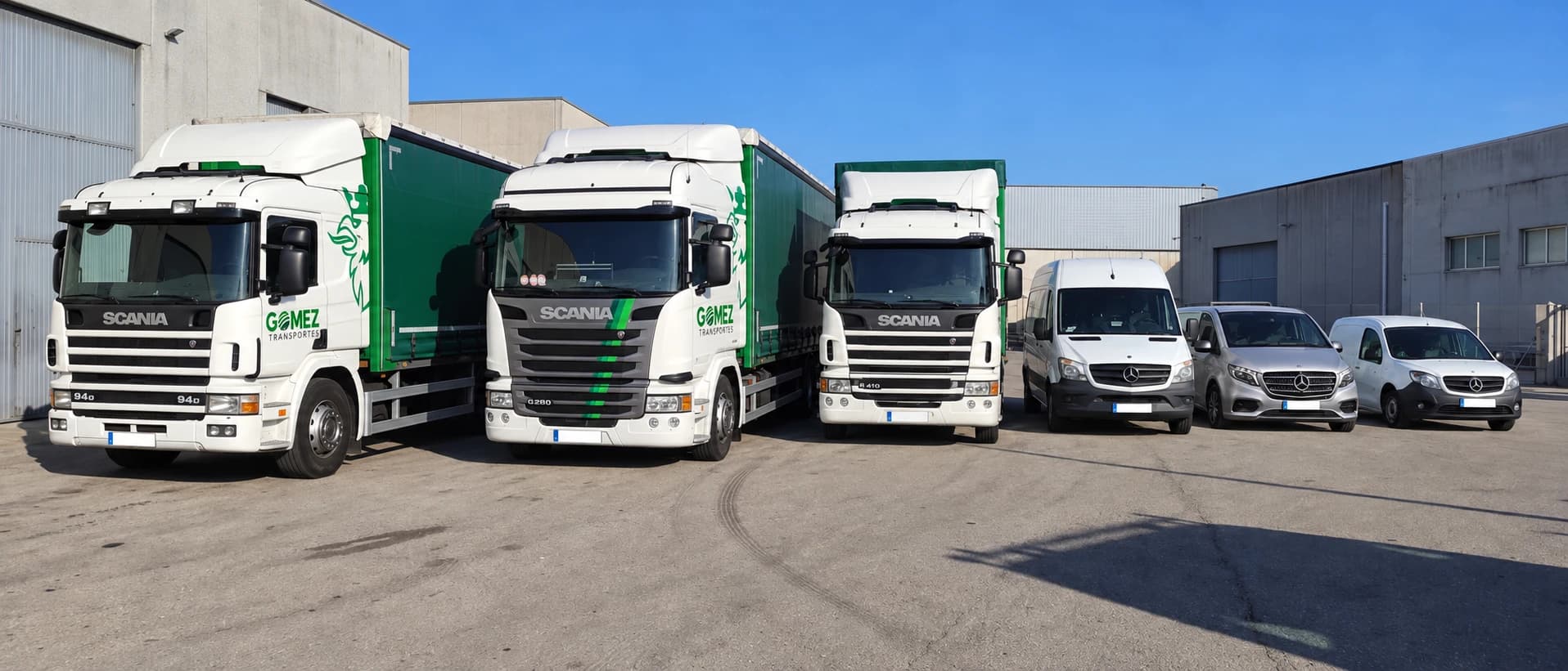 Tres camiones Scania de lona con la rotulación de Transportes Gómez, una Sprinter, una Vito y una Citan frente a una nave